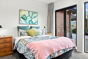 A bedroom with a bed, a nightstand, a lamp, a painting, and a sliding glass door leading to an outdoor area. - Executive family house, private with stunning rural views close to Lake Rotoura (Rotorua)
