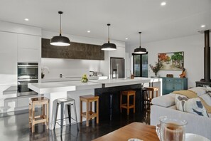 A modern kitchen with a central island, pendant lighting, and a dining area with a sofa and stools. - Executive family house, private with stunning rural views close to Lake Rotoura (Rotorua)