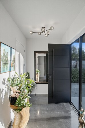 A modern interior with a black door, a hallway, a ceiling light fixture, and a large potted plant. - Executive family house, private with stunning rural views close to Lake Rotoura (Rotorua)