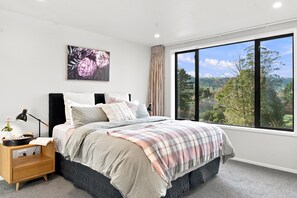 Un dormitorio con un ventanal grande, una cama con manta escocesa, una mesita de noche con lámpara y una obra de arte floral enmarcada en la pared.