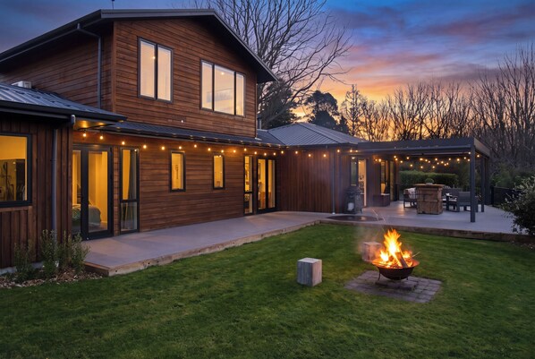 A two-story wooden house with a covered patio and a fire pit in the yard. - Executive family house, private with stunning rural views close to Lake Rotoura (Rotorua)