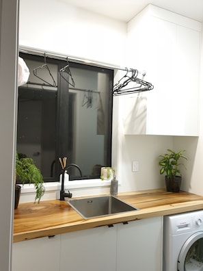 A compact kitchen with a built-in sink, a Bosch washing machine, a window with a black frame, and a drying rack. - Executive family house, private with stunning rural views close to Lake Rotoura (Rotorua)