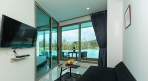 Ein modernes Wohnzimmer mit Fernseher, Sofa, Esstisch mit Obst und einem großen Fenster mit Blick auf einen Pool und Grünflächen.