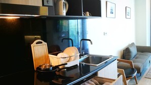 A modern kitchen with a black countertop, stainless steel sink, and wooden cabinets. There is a built-in oven and a coffee maker on the countertop. - Luxury Sea View 1Bedroom Apartment (Kamala)