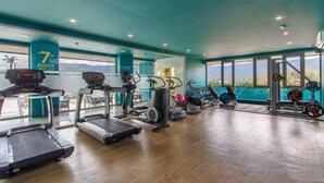 A gym with treadmills, elliptical machines, and weight equipment on a wooden floor with large windows offering a view of the outdoors. - Luxury Sea View 1Bedroom Apartment (Kamala)