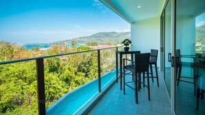 A balcony with a view of the sea and hills, furnished with chairs and a table. - Luxury Sea View 1Bedroom Apartment (Kamala)