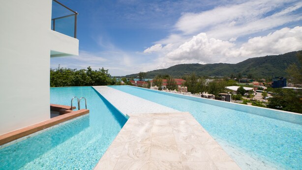 A swimming pool with a clear view of mountains and a modern building in the background. - Luxury Sea View 1Bedroom Apartment (Kamala)