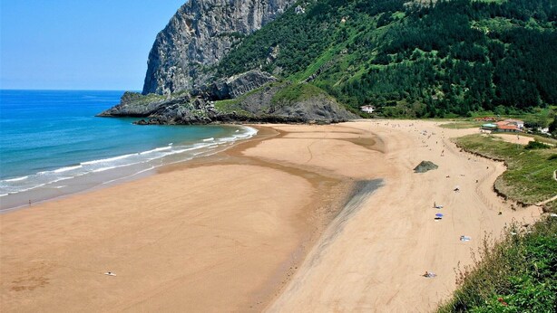 Une plage bordée d’une falaise rocheuse, sous un ciel dégagé.