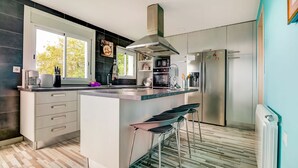 Une cuisine moderne dotée d’un îlot central, d’appareils électroménagers en acier inoxydable et d’une fenêtre laissant entrer la lumière naturelle.