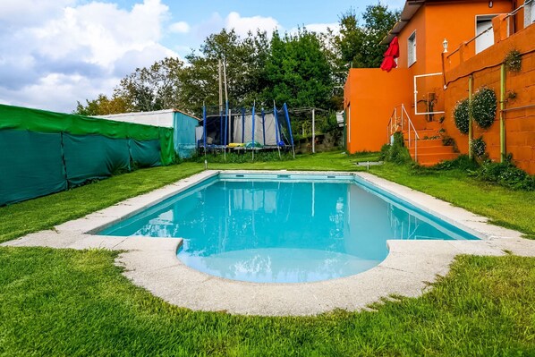 A swimming pool surrounded by a well-maintained lawn, a trampoline, and a building with a red roof. - Holiday Home in Redondela with Sea Views (Chapela)