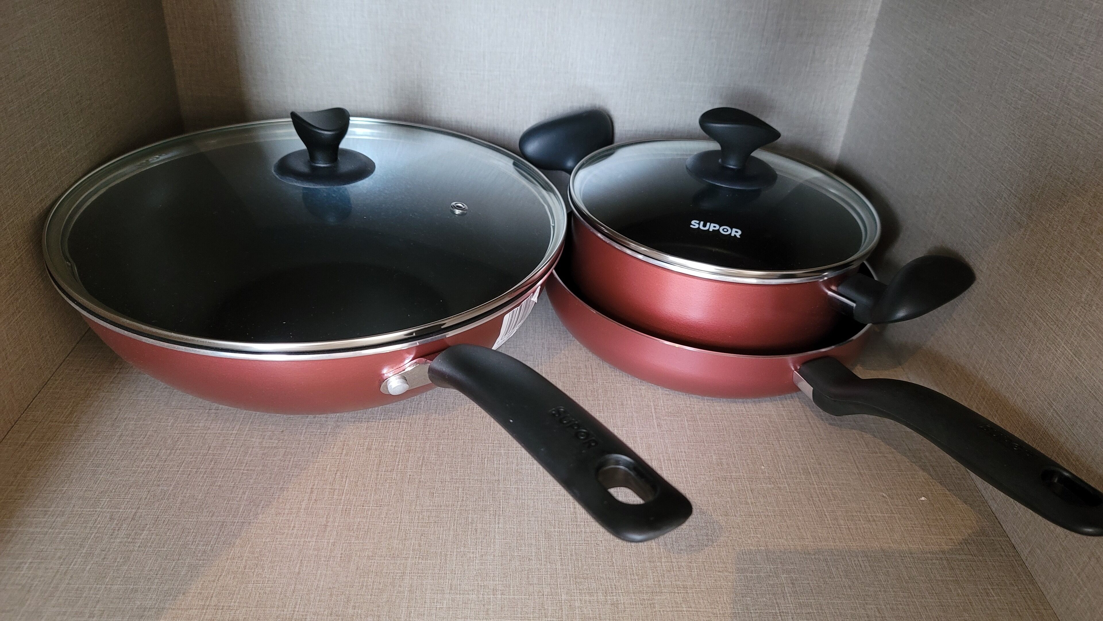 Two red pots with black lids and handles, placed on a beige fabric surface.