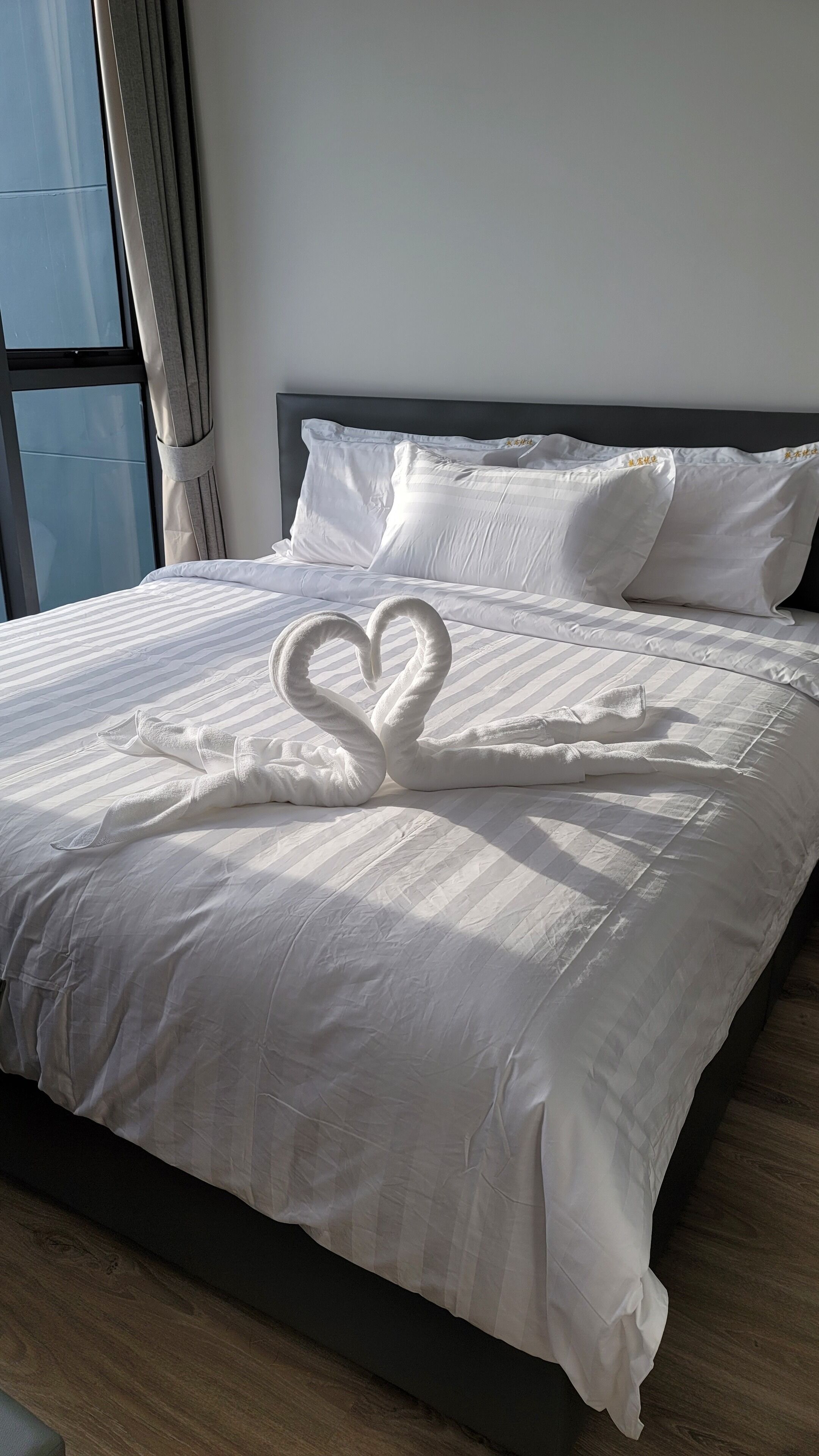 Un lit bien fait, agrémenté d’une décoration en forme de cœur réalisée avec des serviettes sur la couverture.