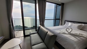 A hotel room with a large bed, a sofa, a small table, and a balcony with a view of the sea. - The Andromeda Condominium (Pattaya)