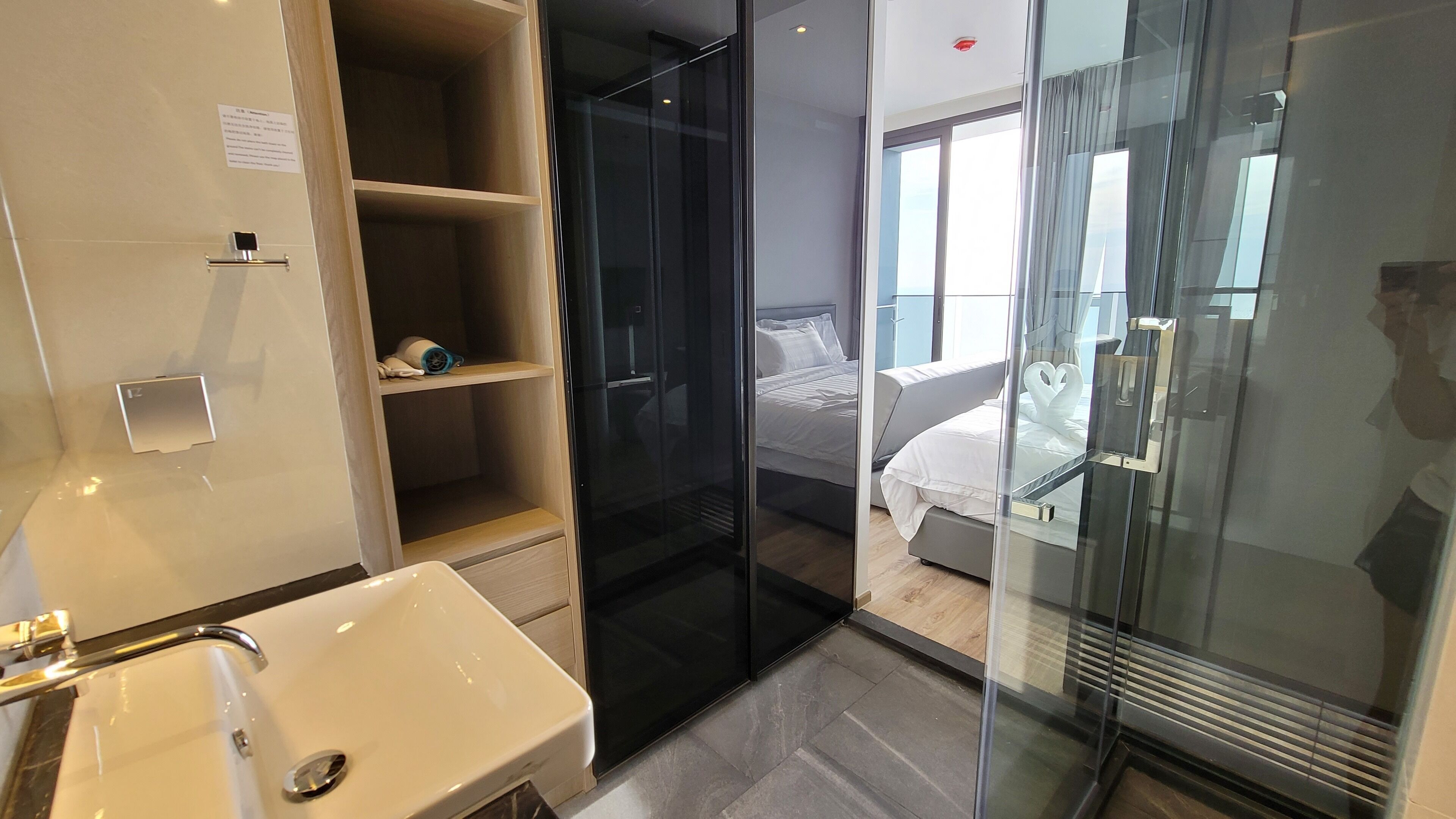 A modern hotel room with a glass shower enclosure, a white sink, and a neatly made bed.
