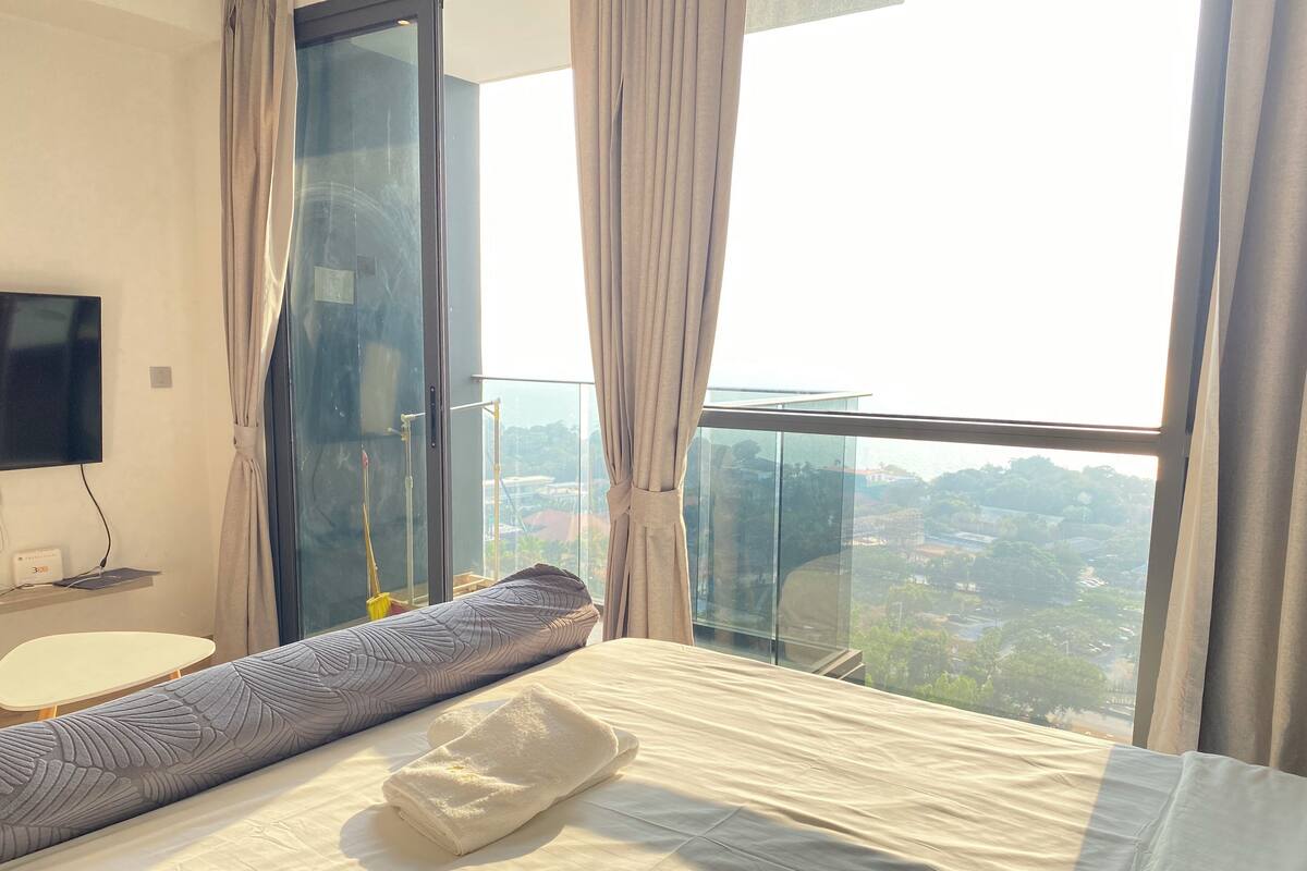 A hotel room with a large bed, a TV, a window with curtains, and a view of the city.