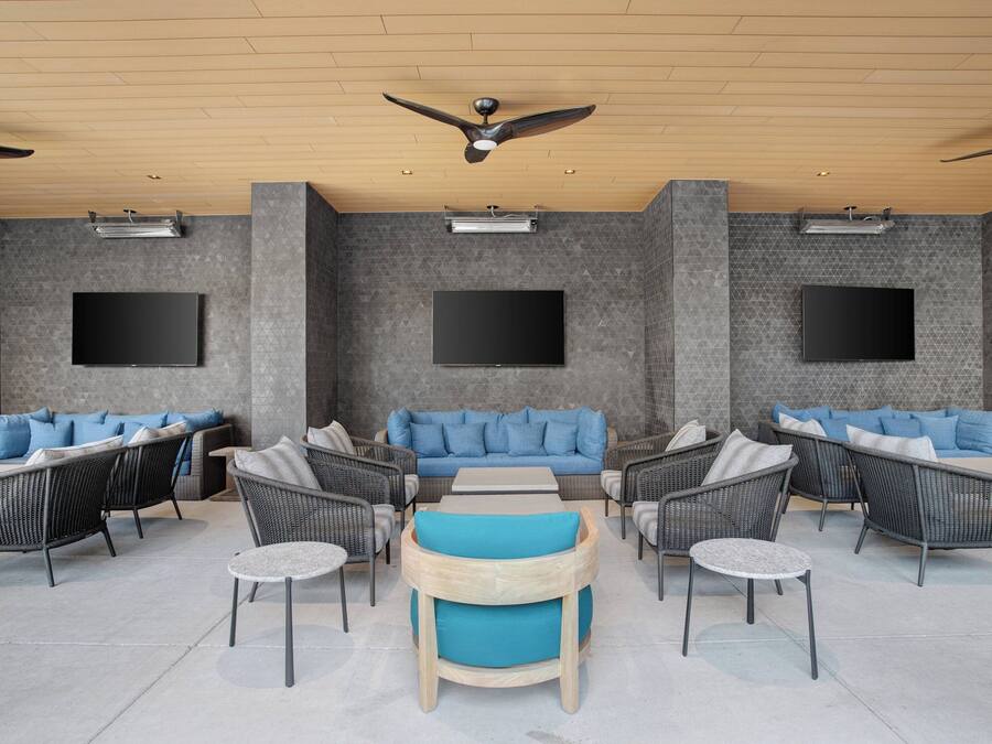An outdoor lounge area with wicker furniture, blue cushions, and a flat-screen TV mounted on the wall.