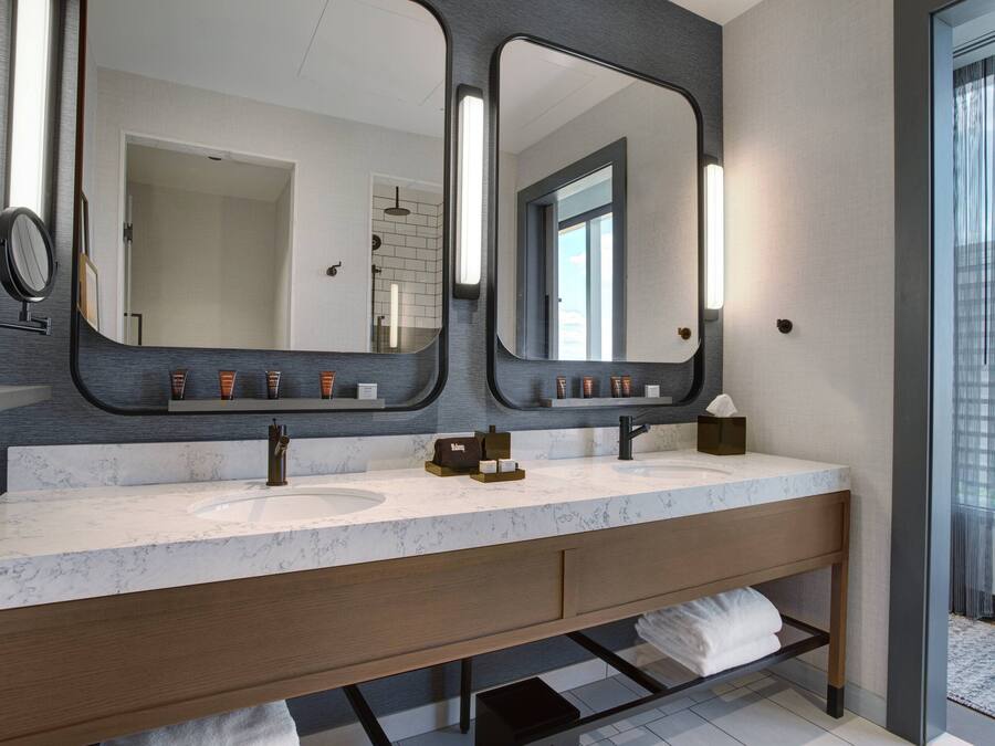 A modern bathroom with a large mirror, dual sinks, and a vanity with a towel rack.
