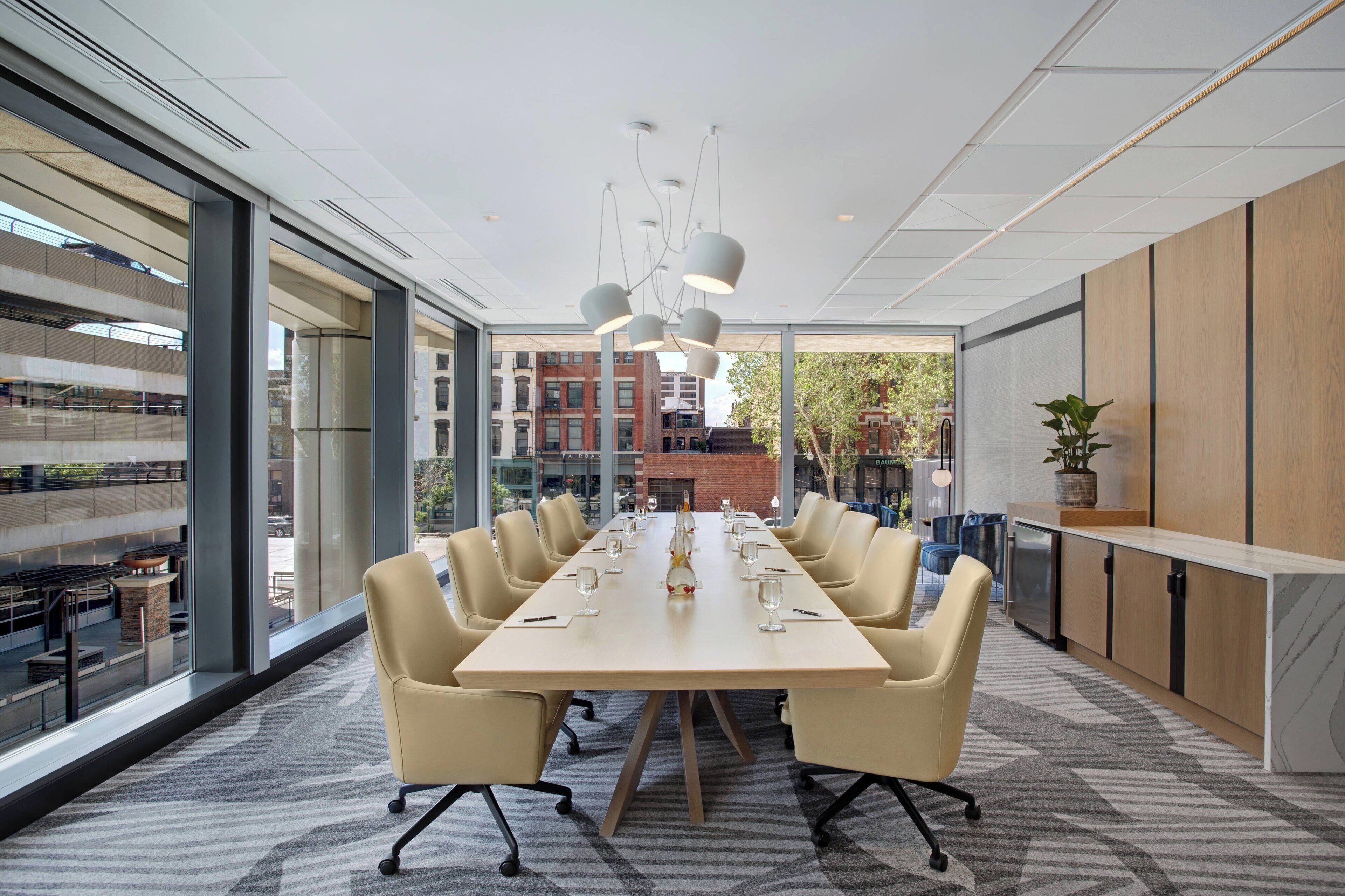 A modern conference room with a long table, comfortable chairs, and a large window offering a view of the cityscape.