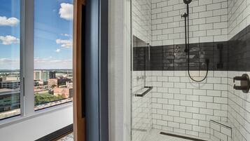 Un baño moderno con azulejos blancos tipo metro, mampara de vidrio y vistas a la ciudad a través de un ventanal grande.