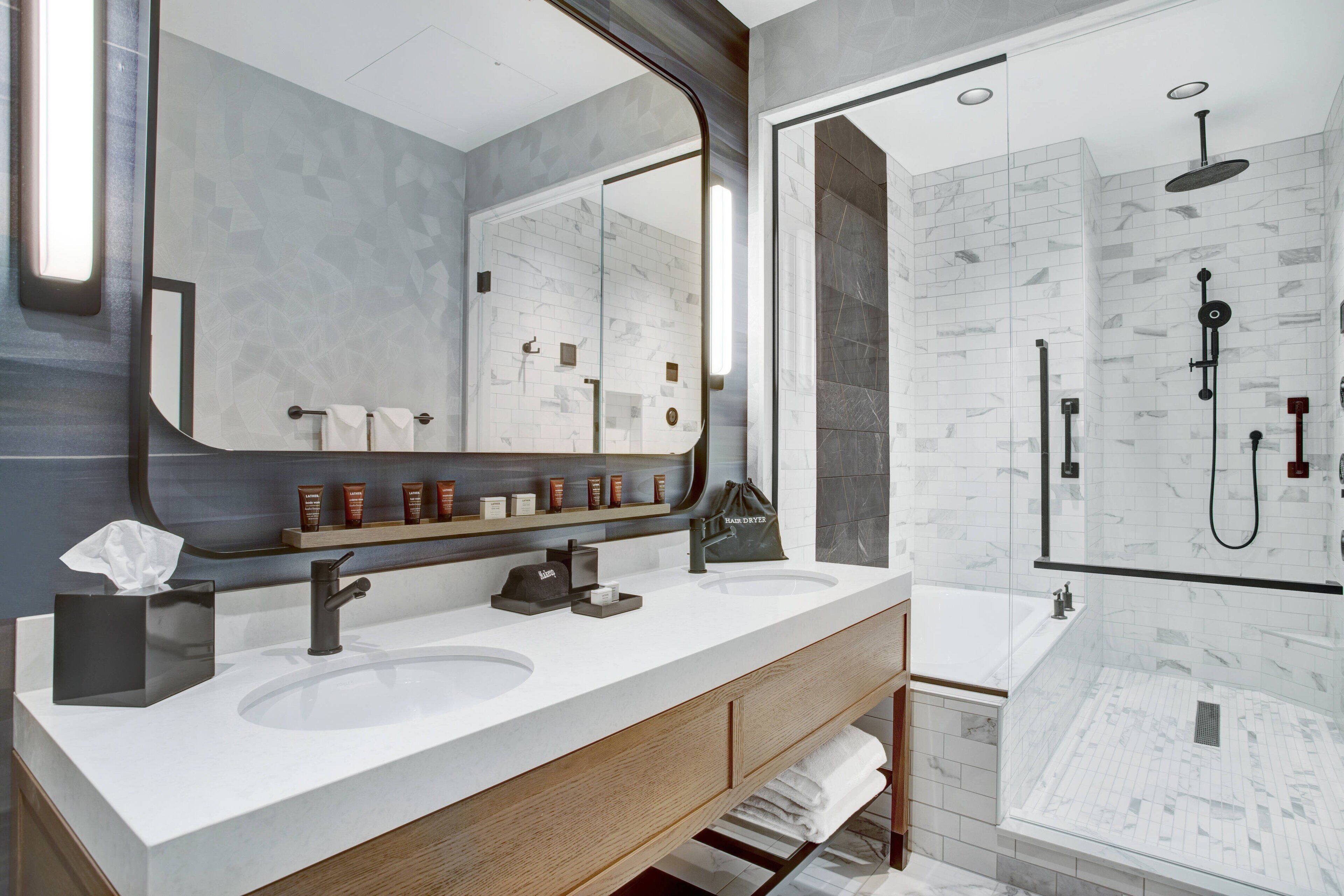 Une salle de bain moderne avec deux lavabos, un grand miroir et une douche séparée par une paroi de verre.
