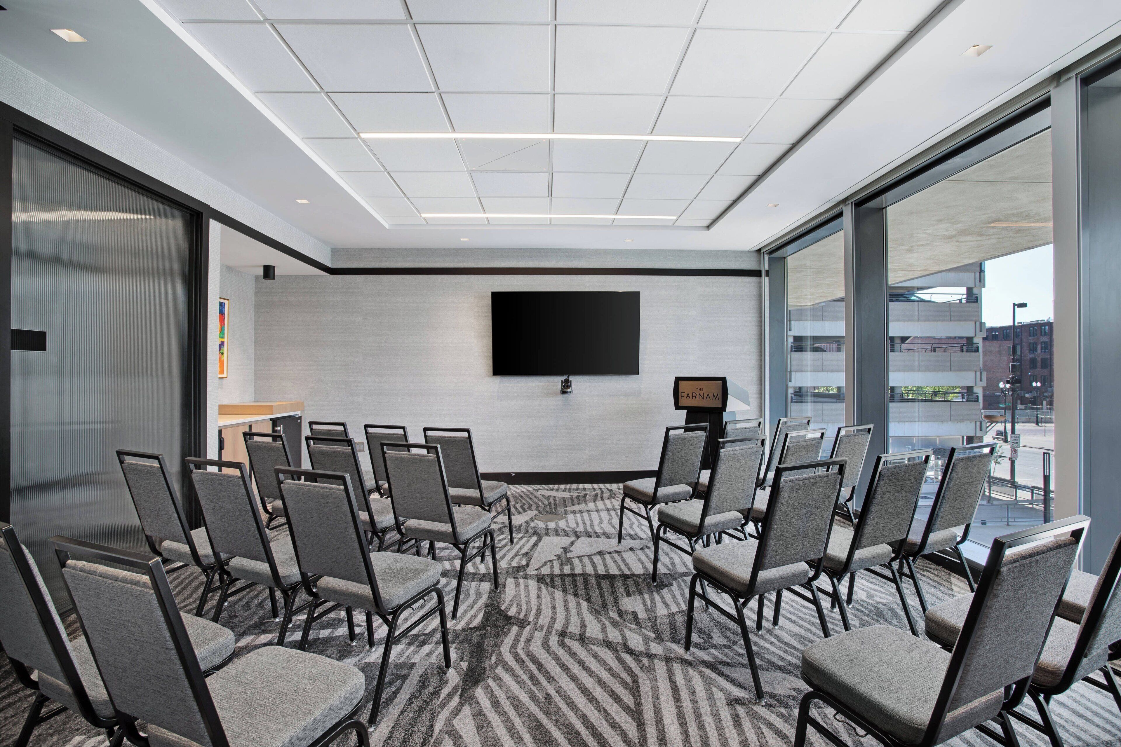 Una sala conferenze con un grande schermo, diverse sedie e un pavimento rivestito di moquette.