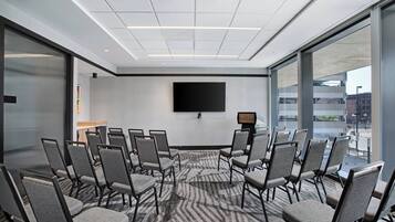 Una sala conferenze con un grande schermo, diverse sedie e un pavimento rivestito di moquette.