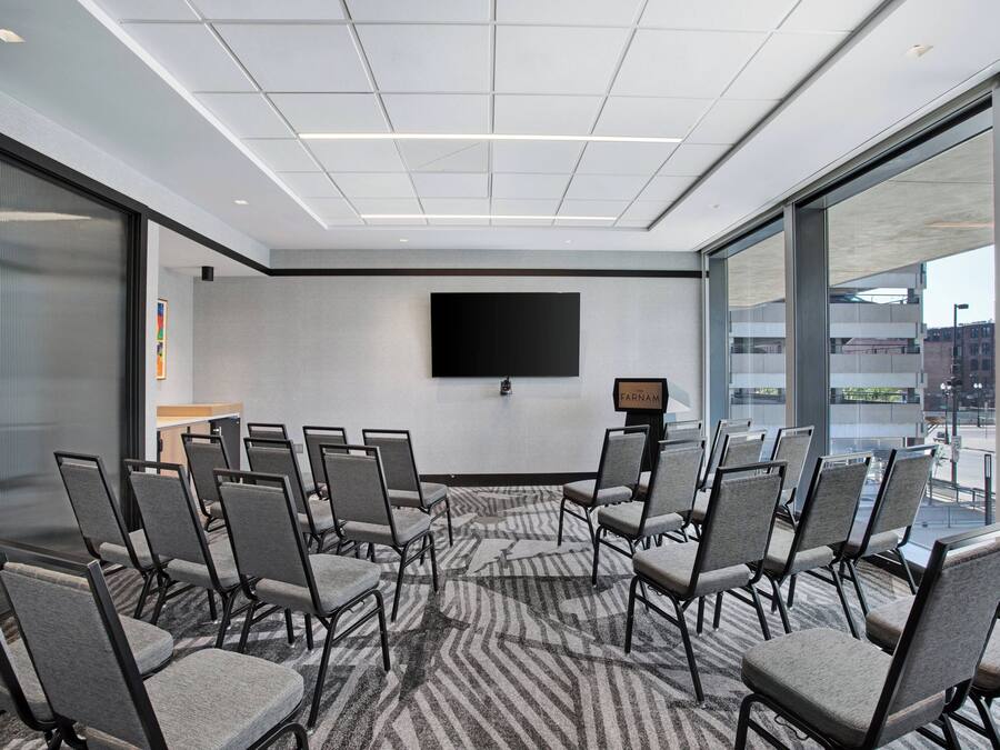 Una sala conferenze con un grande schermo, diverse sedie e un pavimento rivestito di moquette.