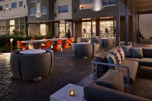 An outdoor seating area with modern furniture, including round tables and sofas, and a glass-topped table with a candle. - Aloft by Marriott Orlando at SeaWorld (Orlando)