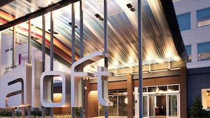 Una entrada de hotel moderna con un llamativo letrero 'HOTEL', amplias ventanas y un vestíbulo cubierto.