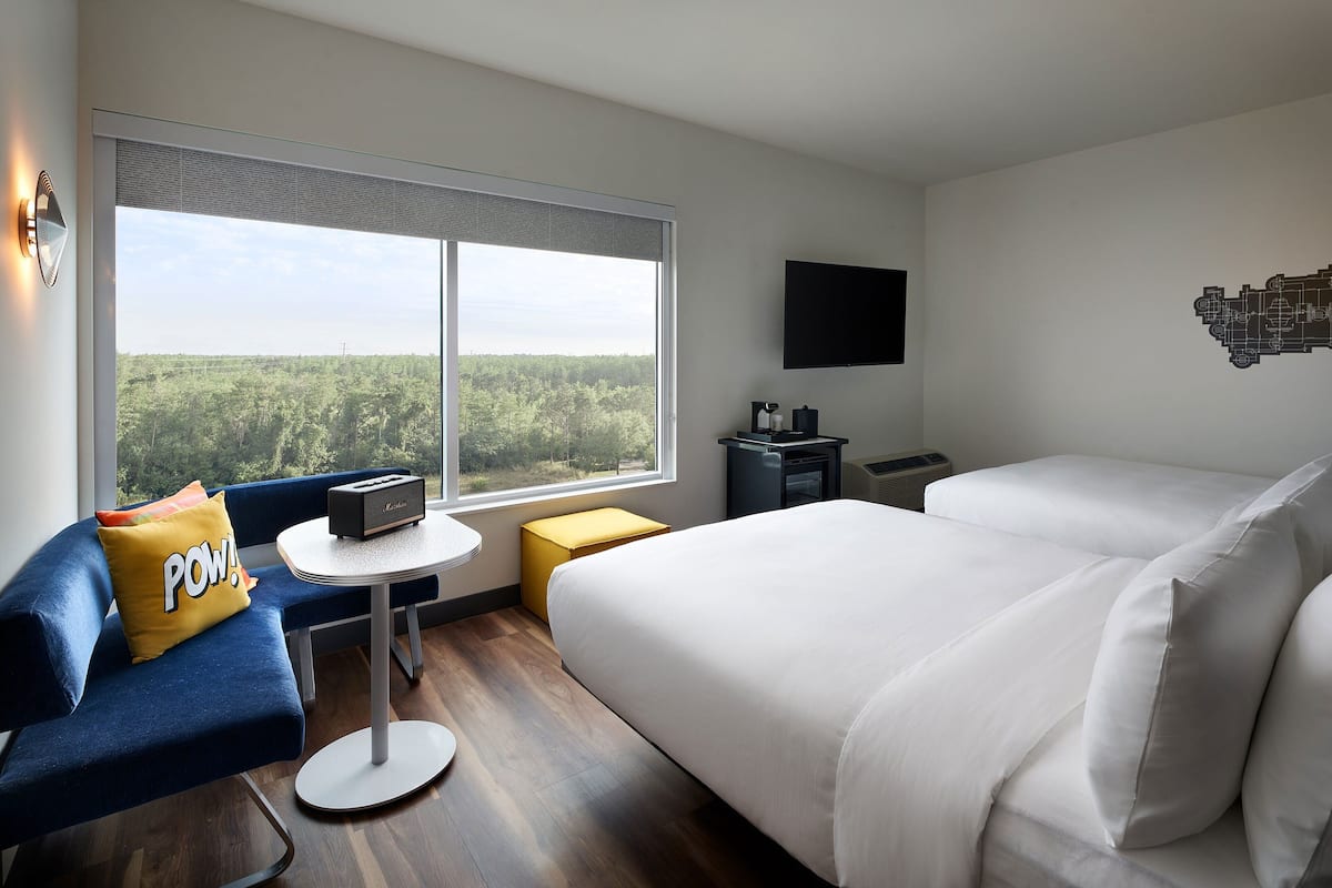 Moderni hotellihuone, jossa on suuri sänky, pieni työpöytä, tuoli ja ikkuna, josta avautuu näkymä metsään.