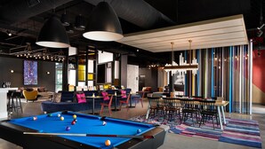 A modern lounge area with a pool table, bar seating, and a colorful striped rug.