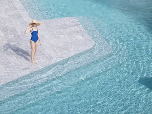 A person in a blue swimsuit standing on a stone ledge by a clear blue pool. - VERSO Hua Hin - a Veranda Collection (Hua Hin)