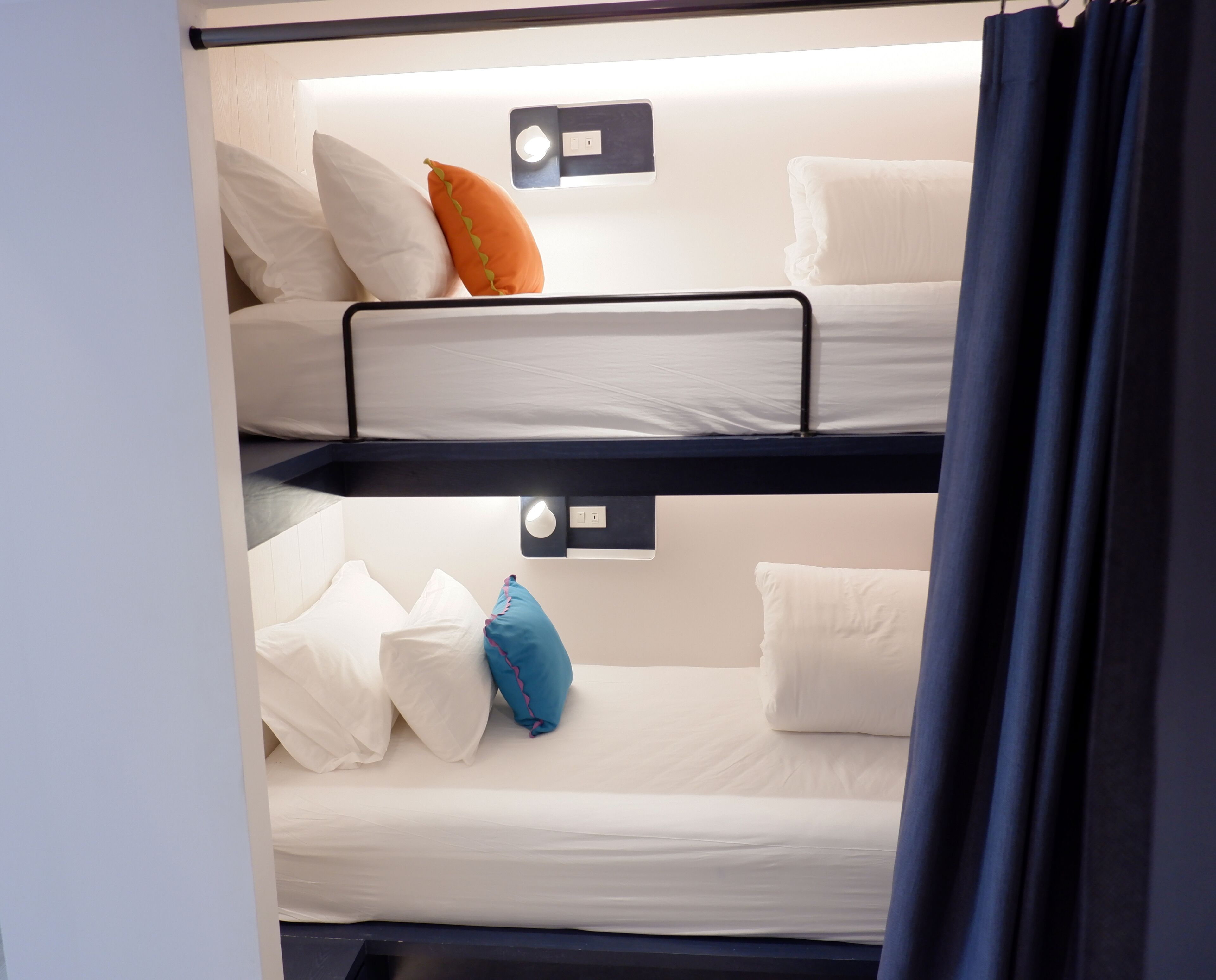 A bunk bed with white bedding and a blue curtain.