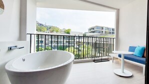 Un baño moderno con una bañera independiente, un balcón con vistas a edificios circundantes y una zona de estar con una mesa y cojines azules.