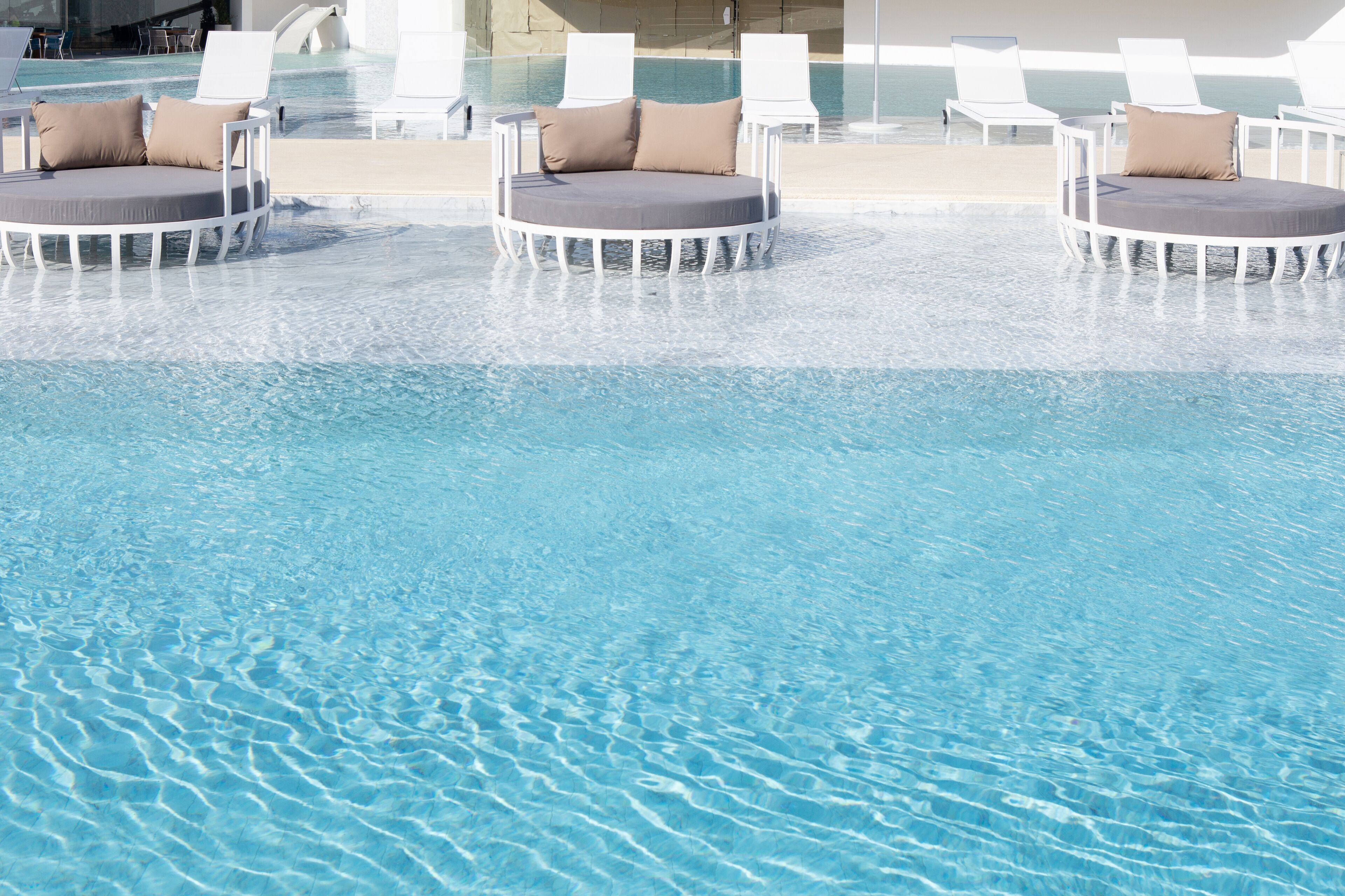 A pool area with three round white lounge chairs, each with a cushion and a pillow.