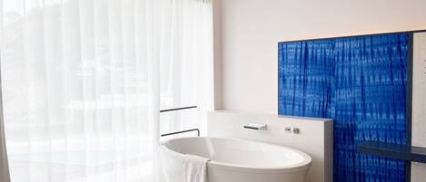 Ein modernes Badezimmer mit einer freistehenden Badewanne, einem runden Tisch mit einem Buch und einem großen Fenster mit transparenten Vorhängen.