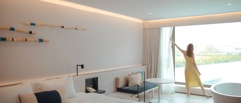 A modern hotel room with a large bed, a seating area with a table, and a view of the outdoors.