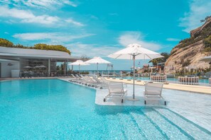 Une piscine entourée de chaises longues et de parasols, le tout niché au cœur d’un paysage rocheux.