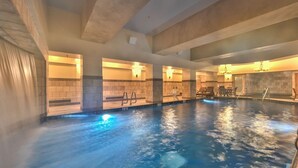Une piscine intérieure à l’eau claire, avec des murs carrelés et un espace détente comprenant des fauteuils et une petite table.