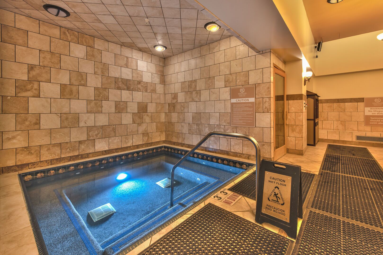 Señal de piso mojado en una habitación con baldosas y una piscina.
