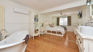 Un dormitorio con una bañera blanca grande, una cama con dosel, un aparador y un tocador con espejo.