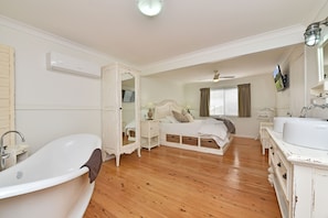 A bedroom with a large white bathtub, a bed with a canopy, a dresser, and a vanity with a mirror.