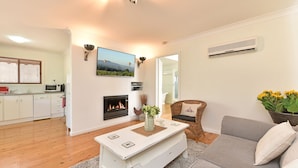 Una sala de estar con chimenea, un televisor montado en la pared y un comedor con mesa blanca.