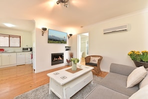 A living room with a fireplace, a television mounted on the wall, and a dining area with a white table.