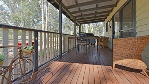 Una terraza de madera con una zona cubierta, mobiliario exterior y una bicicleta.