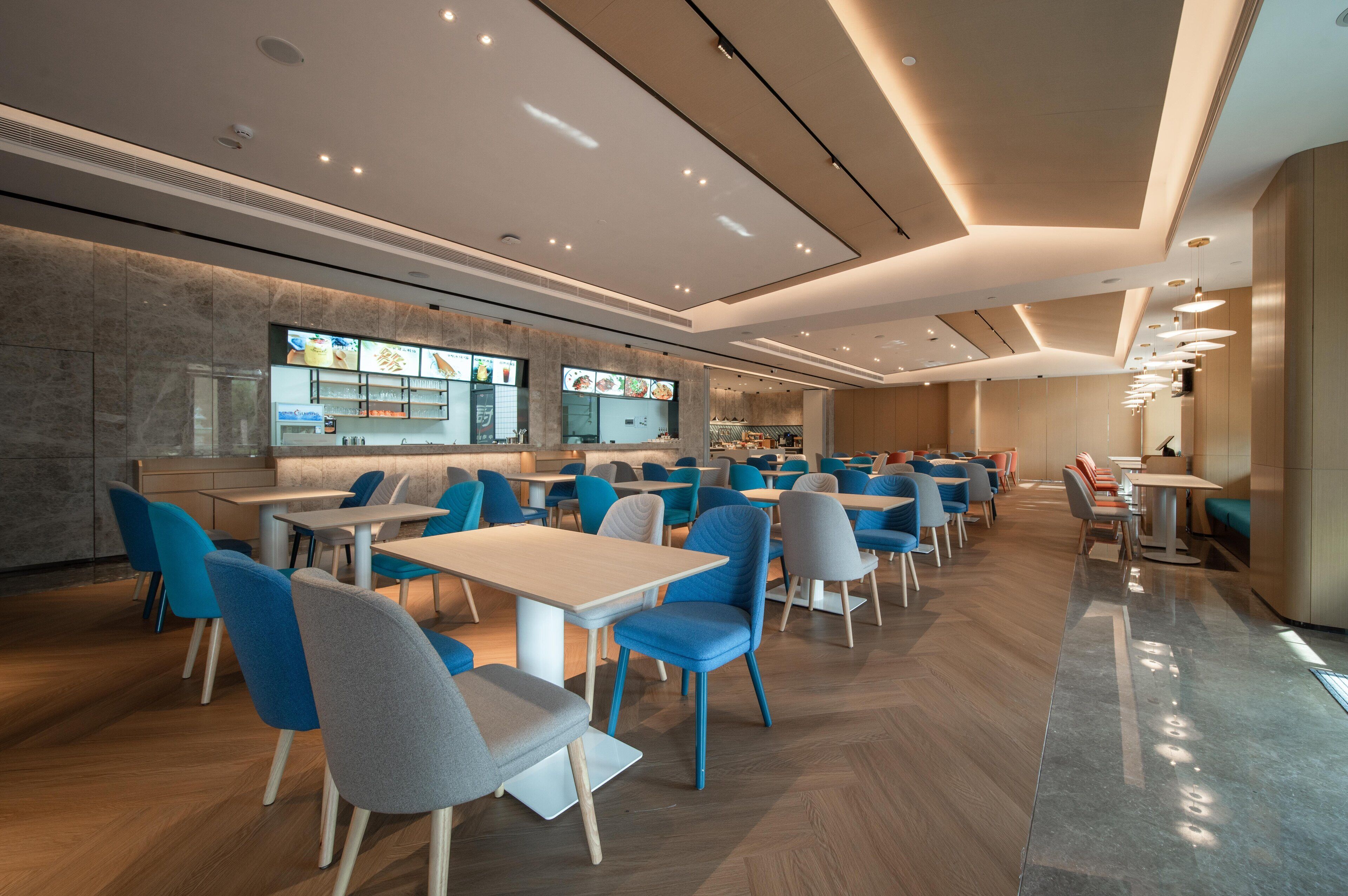 A modern restaurant with multiple dining tables and chairs, a kitchen area, and a menu display.