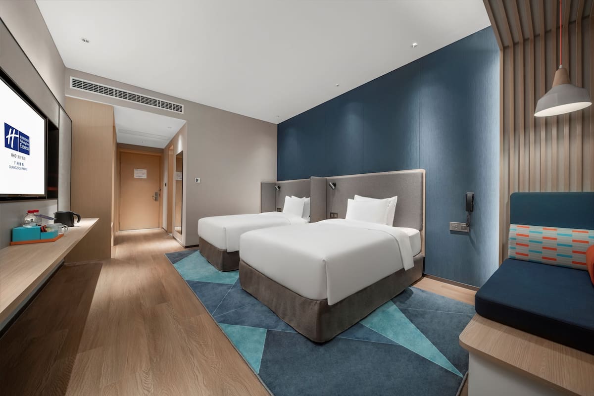 A modern hotel room with two beds, a desk, and a seating area.