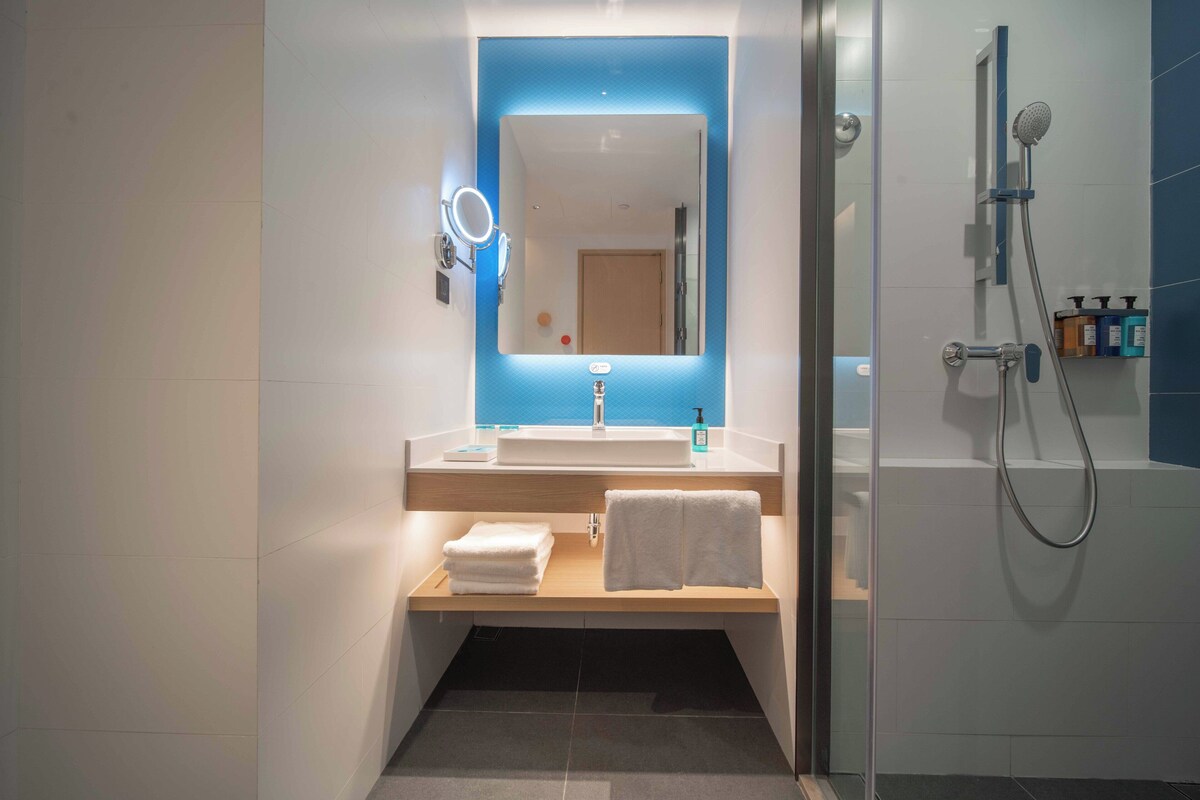Een moderne badkamer met een grote spiegel, een wastafel, een douche en een handdoekrek.