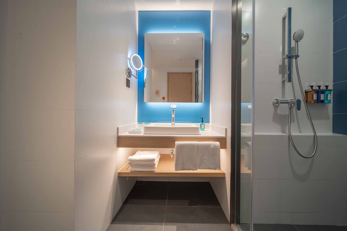 A modern bathroom with a large mirror, a sink, a shower, and a towel rack.