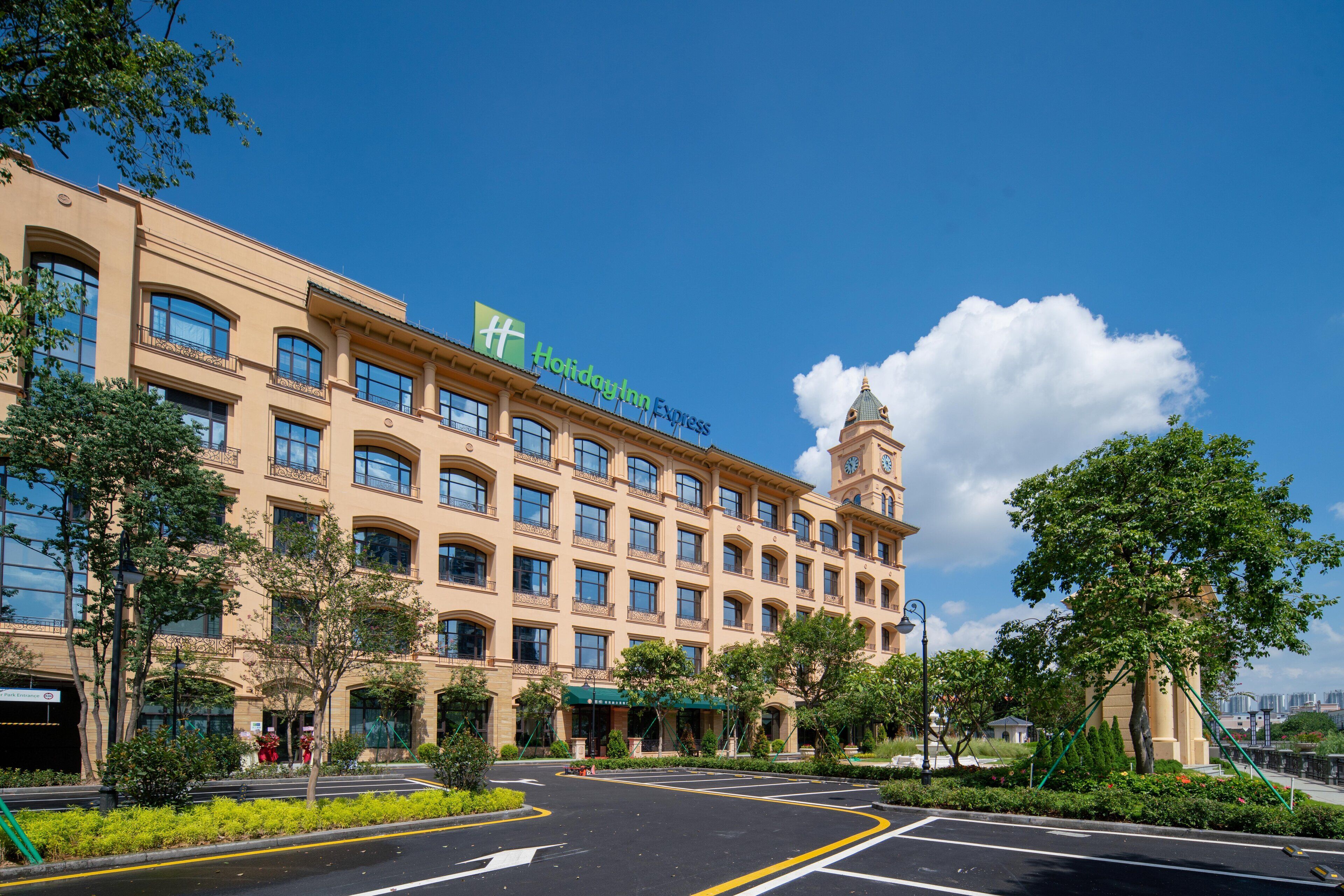 A large hotel with a prominent clock tower, multiple balconies, and a well-maintained garden area.